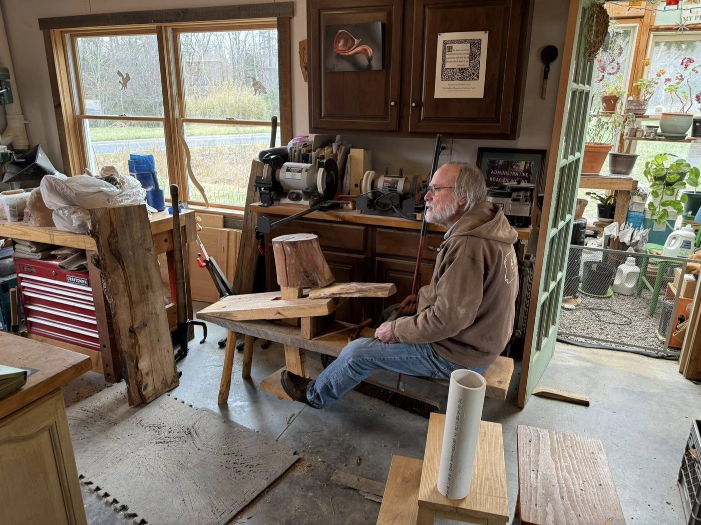 Paul Eisenhauer seated at his shaving horse in his Celo, NC studio, surrounded by lumber stacks, hand tools, and works in progress