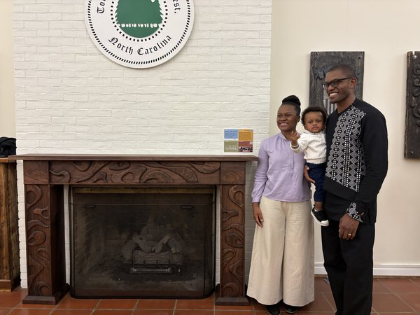 The finished carved black walnut mantel installed at the Biltmore Forest Town Hall hearth, with visitors standing beside it beneath the town seal
