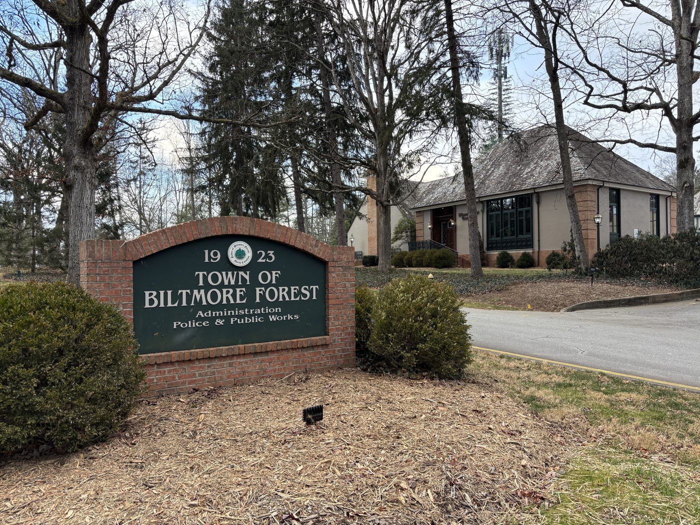 The brick Town of Biltmore Forest sign, established 1923, with Town Hall behind it among bare winter trees