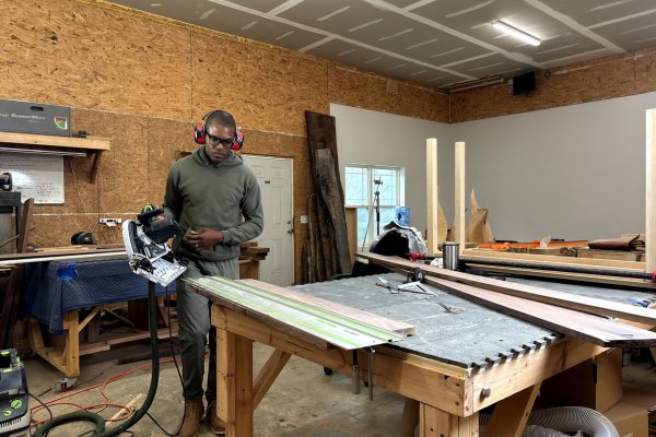 Kwadwo Som-Pimpong with a track saw at a workbench in his workshop, walnut boards laid out for the mantel