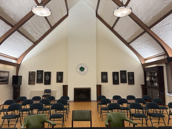 The vaulted interior of Biltmore Forest Town Hall, with the white brick chimney, town seal, and rows of chairs facing the hearth