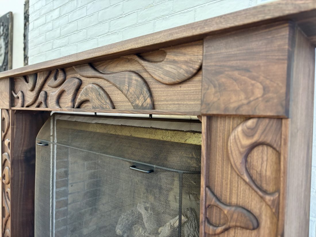 A close-up of the hand-carved black walnut Echo mantel at Biltmore Forest Town Hall, showing the flowing branch and root motifs at an angle