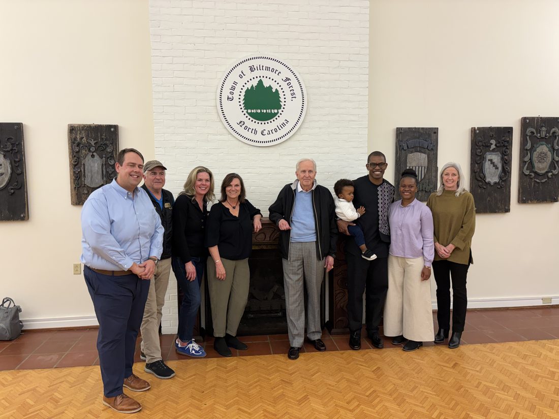 A multigenerational group gathered at the Biltmore Forest Town Hall fireplace beneath the town seal at the Echo mantel dedication