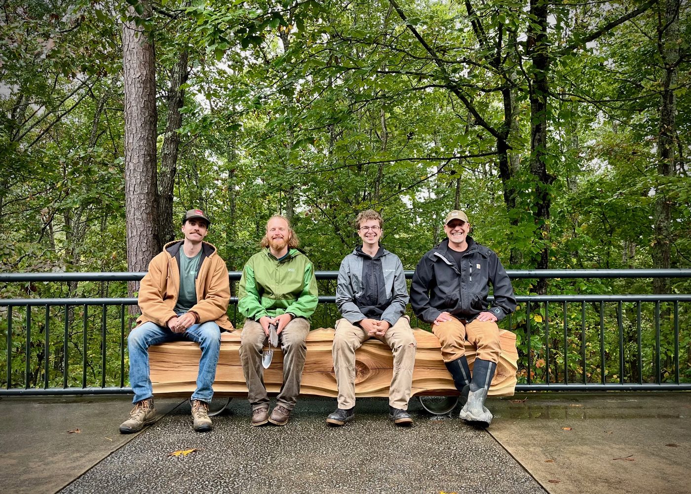 Four men seated together on a hand-hewn log bench commissioned by Echoes of the Forest
