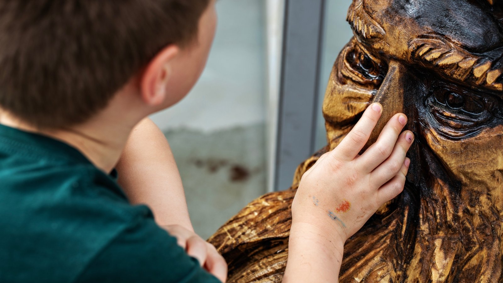 A boy touching an Echoes of the Forest chainsaw-carved wood sculpture