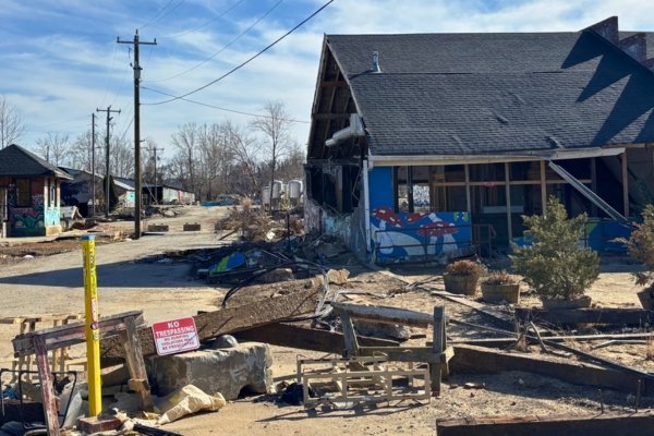 A damaged building in Asheville's River Arts District after Hurricane Helene — a NO TRESPASSING sign in front of a graffitied artist studio with a partially collapsed roof and debris strewn across the gravel street