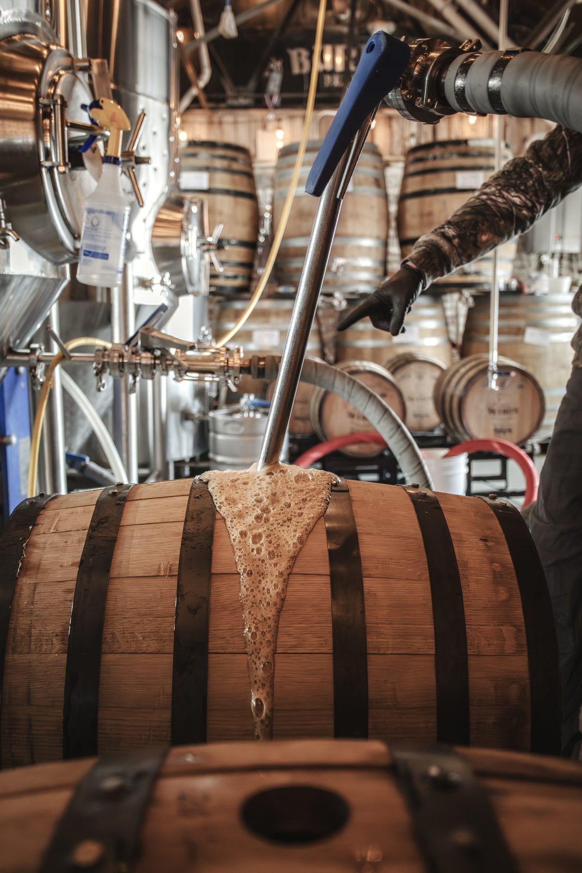 Brown ale flowing through a fill arm and foaming over the bung as it enters one of six Echoes of the Forest oak aging barrels