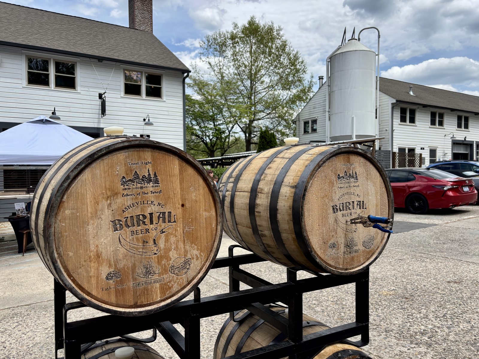 Two branded Echoes of the Forest oak barrels stacked on a rack outside Burial Beer Co.'s Forestry Camp brewery