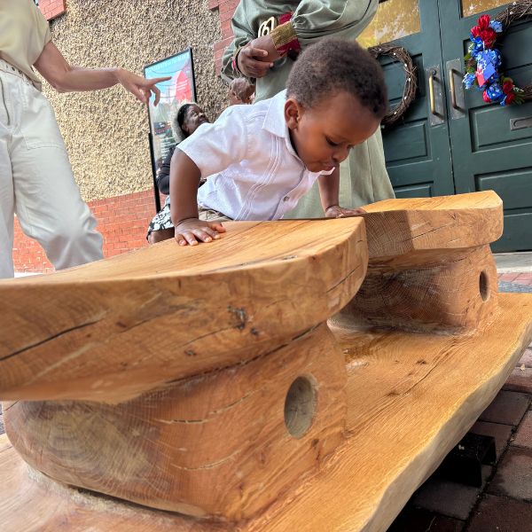 A toddler climbs across the carved seats of the bench