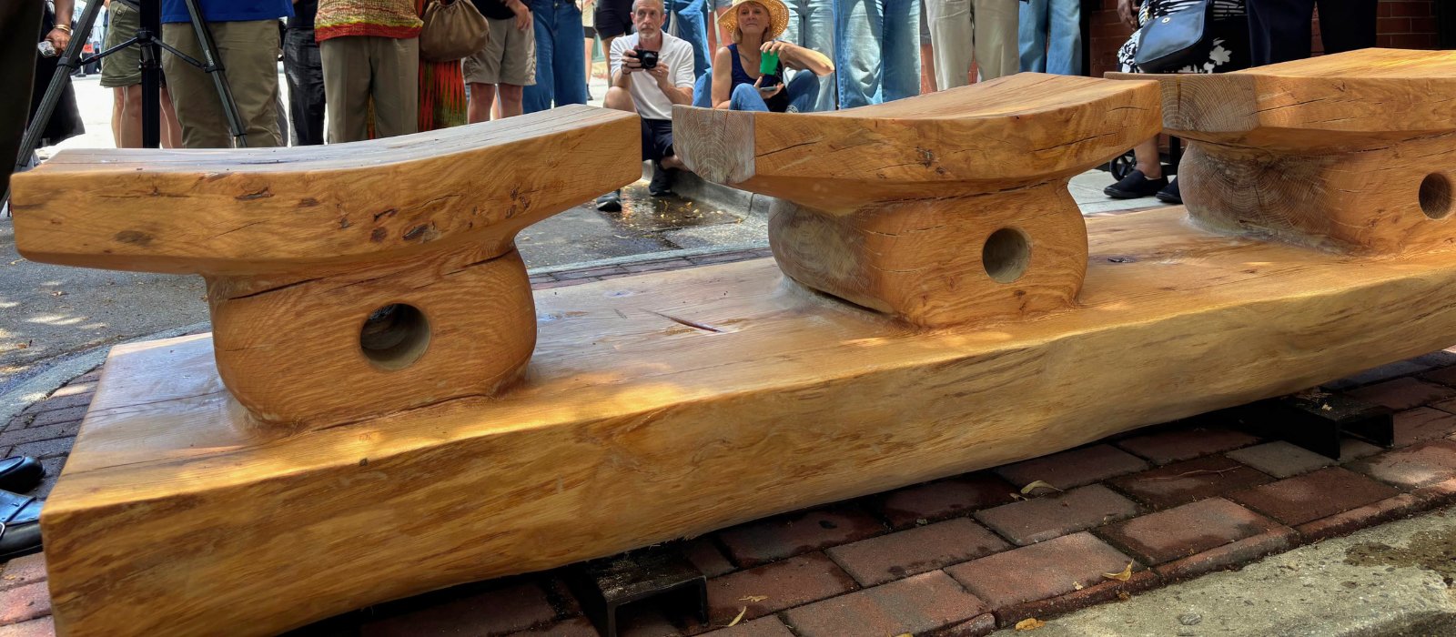 Close view of the white oak bench at the YMI Cultural Center — three carved seats inspired by Ashanti chief stools, with the unveiling crowd behind