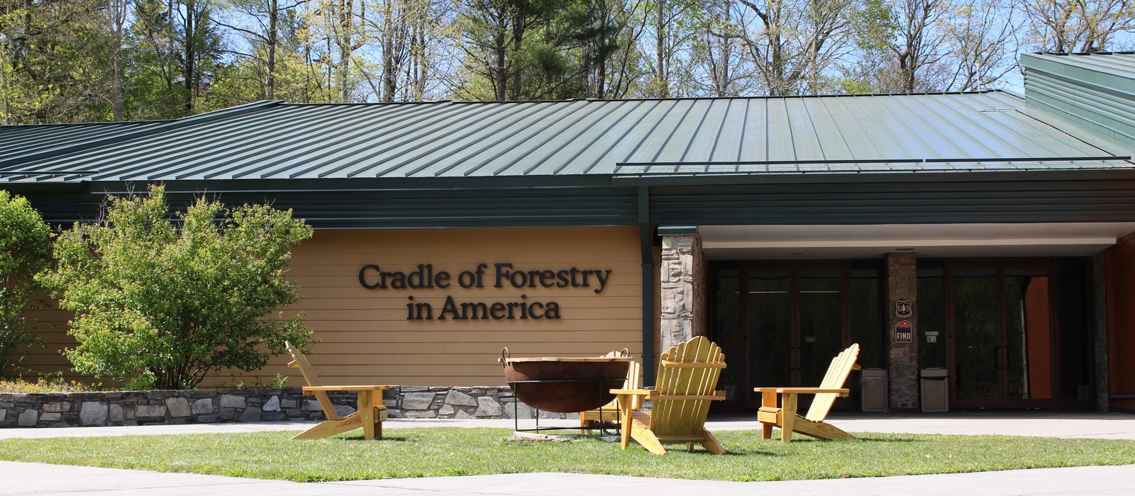 The Cradle of Forestry in America visitor center in Pisgah National Forest, with wooden Adirondack chairs and a fire cauldron on the lawn out front