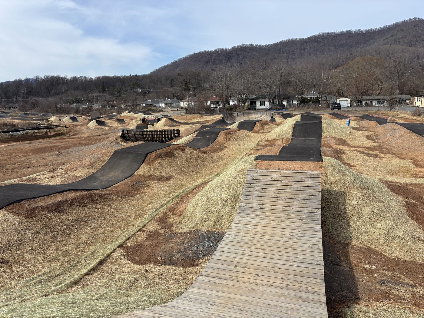 A bike pump track under construction at Beacon Village Park in Swannanoa, with a wooden boardwalk and the surrounding mountains in the background